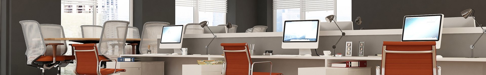 photo of some desks in an office lined up next to each other. each desk has an orange chair and a laptop on top