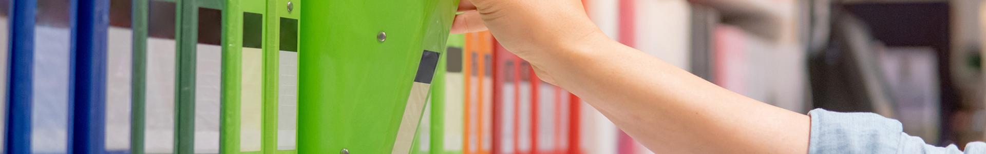 person grabbing a green binder from a shelf of assorted colorful binders