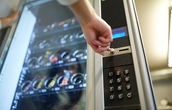 photo of a snack vending machine with a bottom perspective looking up to the machine. an arm is reaching out to press a button on the machine