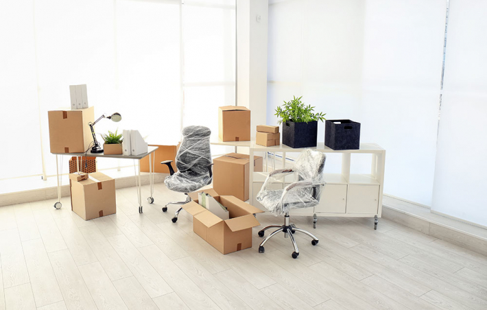 photo of a mostly empty room with a desk and some unopened boxes and wrapped office chairs in the corner