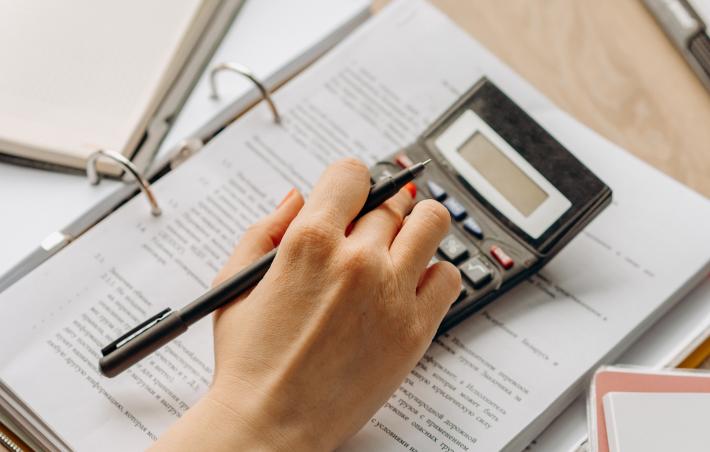 a person uses a calculator with their right hand and is surrounded by office supplies